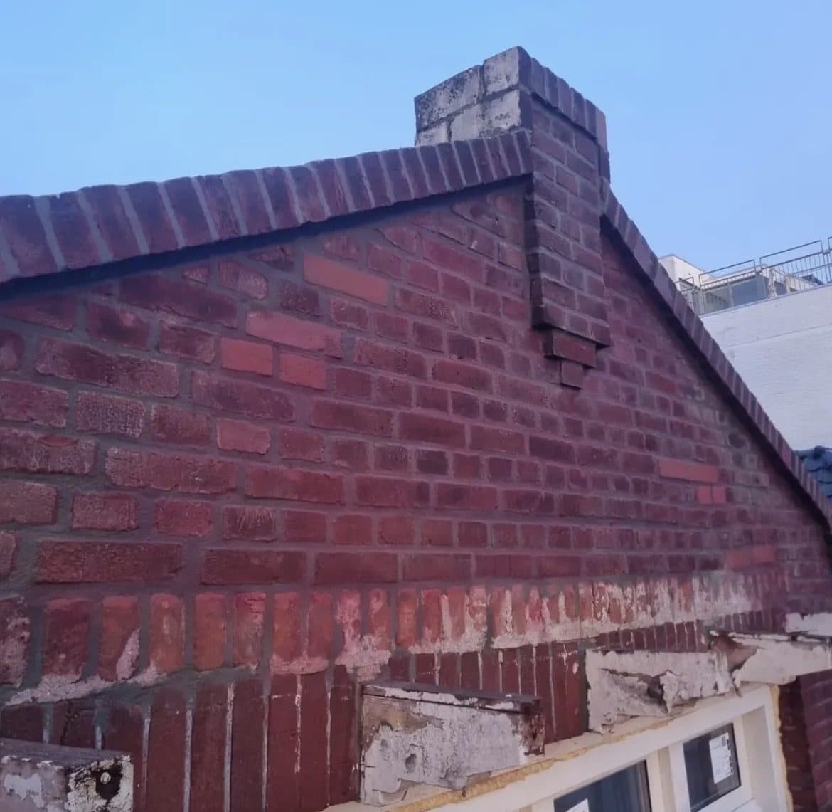 Topgevel van een rijwoning met schoorsteen, met een scheur die vanaf de nok door het metselwerk loopt